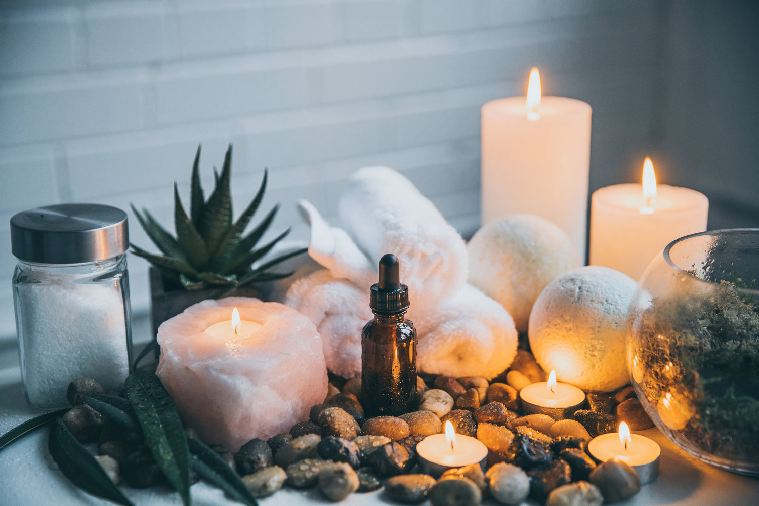 Candlelit scene with rocks, succulents, and a bottle of essential oil on a white surface.